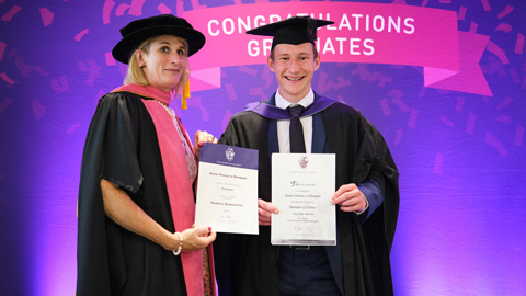 Two people at a graduation ceremony holding certificates.